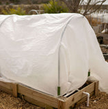 Wooden raised garden bed with a white plastic cover in an outdoor setting
