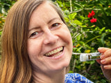 Woman holding a tube of cream in front of a green background with red flowers
