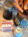 Bar of soap with 'A Slice of the Good Life' branding, jar of honey, and pitcher of milk on a countertop.