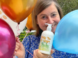 Woman holding a bottle of White Tea & Ginger product with balloons in the background