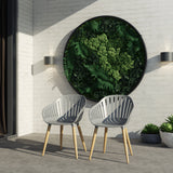Two modern chairs on a patio with a circular wall art piece featuring greenery.