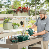 Man watering plants in a garden setting with a focus on gardening tools and plants.
