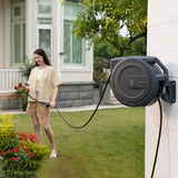 Woman using a hose connected to a wall-mounted hose reel in a garden setting.