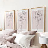 Three framedPink Wall Art Set Of 3 Botanical Modern Decor on a wall above a bed with pink and white bedding.