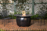 Fire pit table with flames in a garden setting with chairs and lattice background
