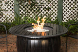 Outdoor fire pit table with flames burning on a patio with lattice fence and plants in the background.