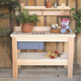 Wooden potting bench with gardening tools and plants against a wooden wall.