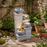 Outdoor garden fountain with stone design, surrounded by plants and stones.