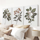 Three botanical wall art pieces above a bed with pillows and a lamp.