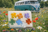 Colorful flower-shaped FLOWER CHILD SOAP SLICE 5.5 oz. with a vintage van in a field of flowers.
