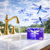 Gold faucet with water flowing, purple soap bar with dragonfly design, and blue dragonflies in the background.