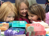 Three children looking at colorful soap bars on a table