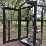 Janco Indoor/Outdoor Garden Cabinet on a wooden deck with plants and decor, surrounded by trees.