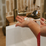 Hand holding a bar of soap with a sink and faucet in the background Agave Products