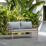 Gray outdoor sofa with wooden frame in front of green plants Eve FSC Teak Outdoor Conversation Set with Cushions