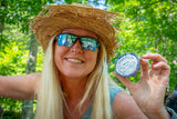 Person wearing a straw hat and sunglasses, holding a OLD FASHIONED MEN'S SHAVE SOAP outdoors with greenery in the background