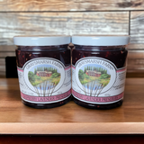 Two jars of raspberry lavender preserves from Graysmarsh Farm on a wooden surface with a wooden background.
