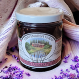 Jar of raspberry lavender preserves from Graysmarsh Farm on a textured fabric background with flowers.