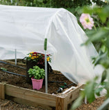 DIY Portable Low Tunnel Kit with plants inside, covered with a white sheet, in a garden setting.