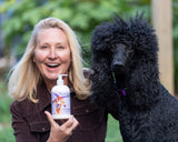 Woman holding a bottle of LAVENDER GOATS MILK LOTION  next to a black dog outdoors.