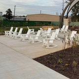 White Savannah Adirondack Rockers arranged on a concrete patio with a building and trees in the background