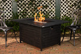 Black fire pit table with flames on a brick patio, surrounded by chairs and a lattice fence.