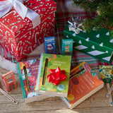 Assorted gift items including books and small boxes on a wooden surface with a Christmas tree in the background. Seed Library