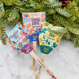 Colorful seed pop packaging with wooden sticks against a snowy background Seed Pops - Pollinator