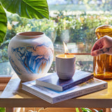 Candle being lit on a book with a vase and plant in the background Garden Vibes Candle/Planter 2-in-1