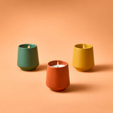 Three colorful candles in ceramic holders on a peach background Rooted Candles