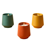 Three colorful candles in green, orange, and yellow containers on a white background Rooted Candles Planters