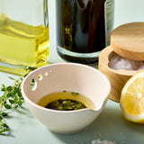 Peel, Grate & Prep Dish with olive oil and herbs, next to a bottle of olive oil, lemon, and wooden container on a light green background.