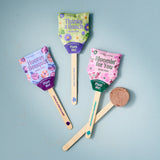 Three colorful seed pop packaging on wooden sticks with a blue background