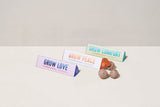Three small cardboard boxes with 'Grow Love', 'Grow Comfort', and 'Grow Peace' text on a light background. Bright Side Seed Balls