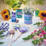 Garden-themed items including potted plants, seed packets, and gardening tools on a wooden surface. Seed Bombs