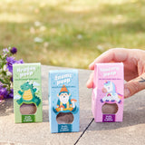 Three colorful boxes of wildflower seed balls held by a hand with a blurred natural background.