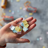 Hand holding small colorful paper squares with a blurred background Seed Confetti Popper