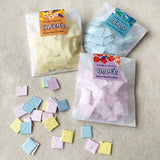 Three packages of flower seed confetti with scattered confetti pieces on a textured surface