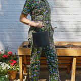 Person wearing a floral apron holding a black pot in front of a raised garden bed.