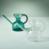Two Glass Watering Cans, one green and one clear, on a light gray background