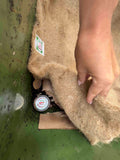 Hand holding a burlap bag with a small container inside, against a green background.