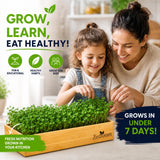 A woman and a young girl smile while looking at and touching a wooden tray filled with fresh green sprouts in a bright kitchen setting. Promotional text reads 'GROW, LEARN, EAT HEALTHY!' and 'GROWS IN UNDER 7 DAYS!' with icons for fun, educational value, healthy habits, and kids.