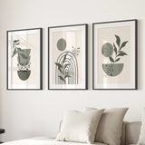 Three framed prints with abstract designs of plants and arches on a wall above a sofa.