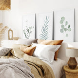 Cozy bedroom with a bed, pillows, and Watercolor Botanical Set of 3 Prints Wall Decor featuring green leaf designs.