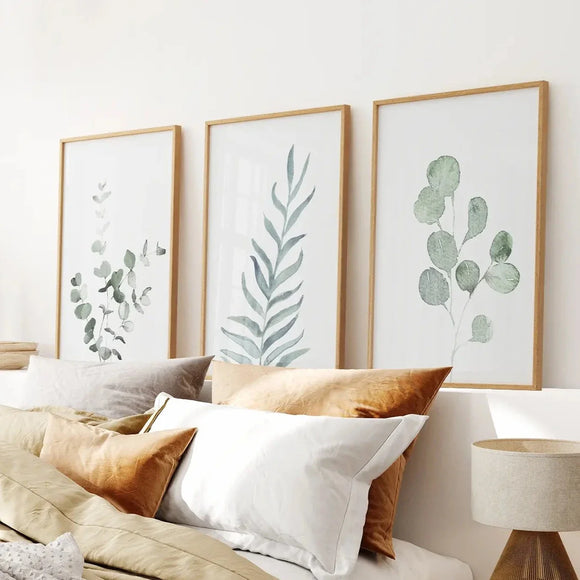 Three framed Watercolor Botanical Set of 3 Prints Wall Decor on a wall above a bed with pillows and a lamp.