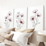 Three floral wall art pieces on a white wall above a bed with pillows and a lamp.