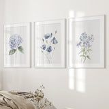 Three framed floral prints on a wall with a soft focus on the bed in the foreground.