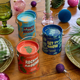 Decorative tins with festive designs on a wooden table with Christmas ornaments.