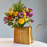 Brass watering can with a colorful bouquet of flowers on a light surface and gray background