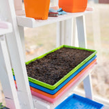 Stack of colorful seedling trays with soil on a white chair.